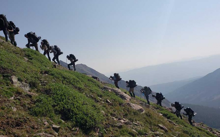 a group of gap year students hike up a grassy incline on an outward bound semester